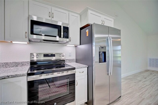 kitchen featuring white cabinets, appliances with stainless steel finishes, vaulted ceiling, and light stone countertops