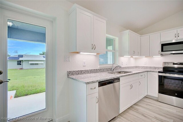 kitchen with white cabinets, stainless steel appliances, vaulted ceiling, and sink