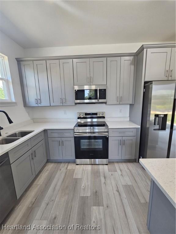 kitchen with light stone countertops, sink, light hardwood / wood-style floors, gray cabinets, and appliances with stainless steel finishes