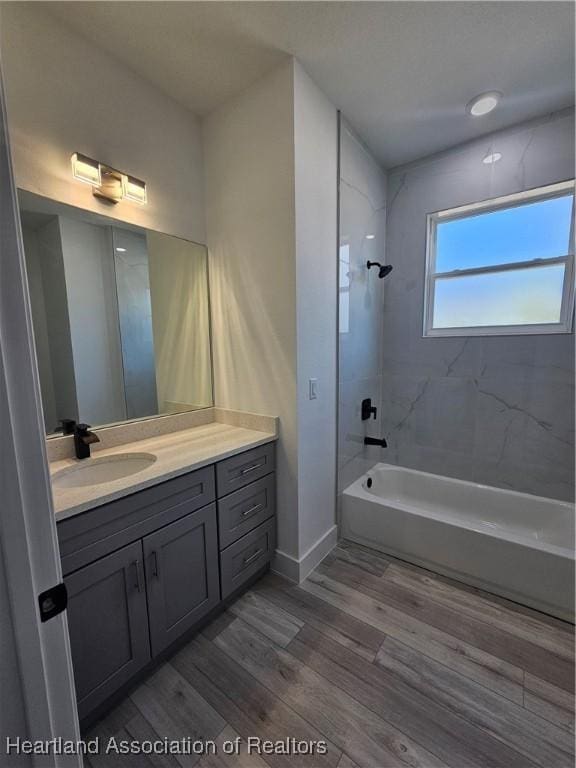 bathroom with hardwood / wood-style flooring, vanity, and tiled shower / bath