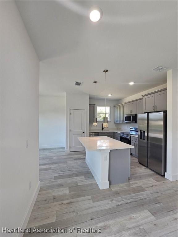 kitchen with gray cabinetry, a center island, light hardwood / wood-style flooring, appliances with stainless steel finishes, and decorative light fixtures