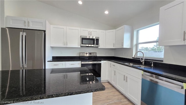 kitchen with lofted ceiling, sink, white cabinetry, dark stone countertops, and stainless steel appliances