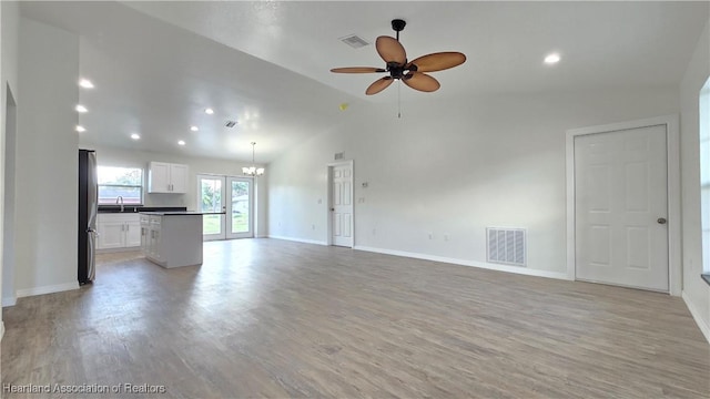 unfurnished living room featuring ceiling fan with notable chandelier, lofted ceiling, sink, and light wood-type flooring