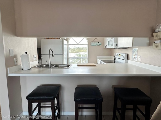 kitchen featuring freestanding refrigerator, a peninsula, a breakfast bar, a sink, and range with electric cooktop