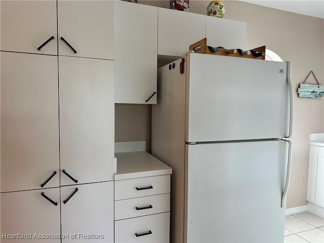 kitchen with white cabinetry, light tile patterned floors, light countertops, and freestanding refrigerator