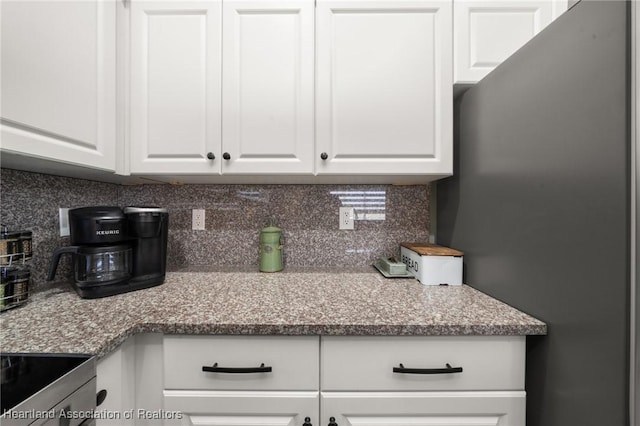 kitchen with white cabinetry, decorative backsplash, light stone countertops, and freestanding refrigerator