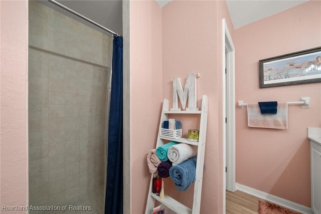 bathroom with vanity, wood finished floors, baseboards, and a tile shower