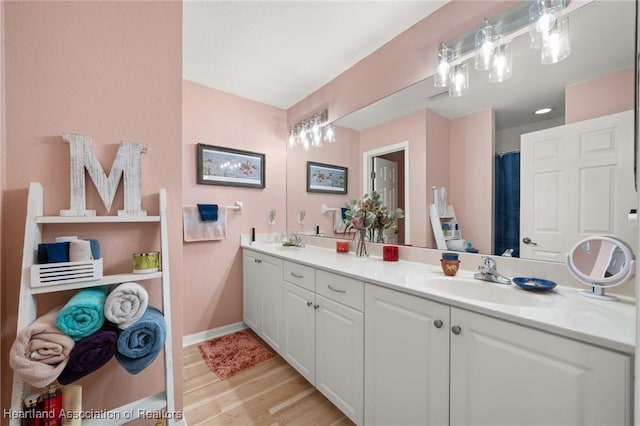 bathroom with double vanity, wood finished floors, baseboards, and a sink