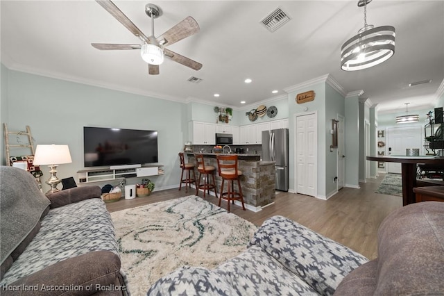 living room featuring dark wood-type flooring, crown molding, a ceiling fan, and visible vents