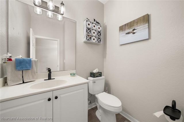 half bathroom with vanity, toilet, wood finished floors, and baseboards