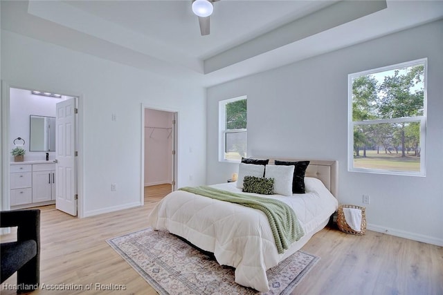 bedroom with baseboards, light wood finished floors, a walk in closet, and a raised ceiling