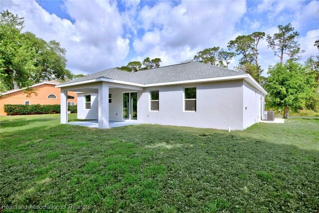 back of property with cooling unit, stucco siding, roof with shingles, a patio, and a yard