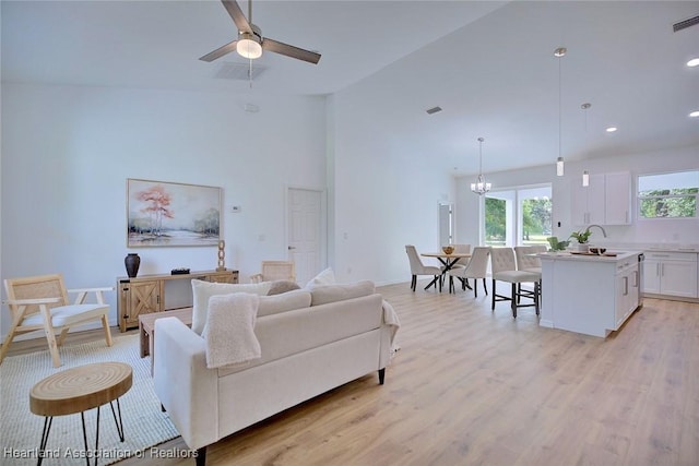 living room featuring a towering ceiling, light wood-type flooring, visible vents, and ceiling fan