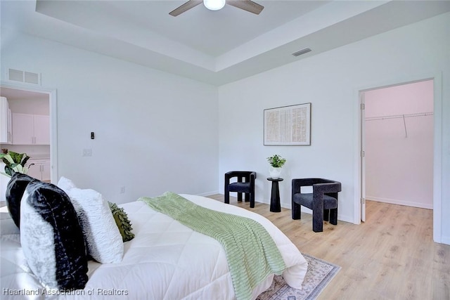 bedroom with light wood-style flooring, visible vents, a walk in closet, and a raised ceiling