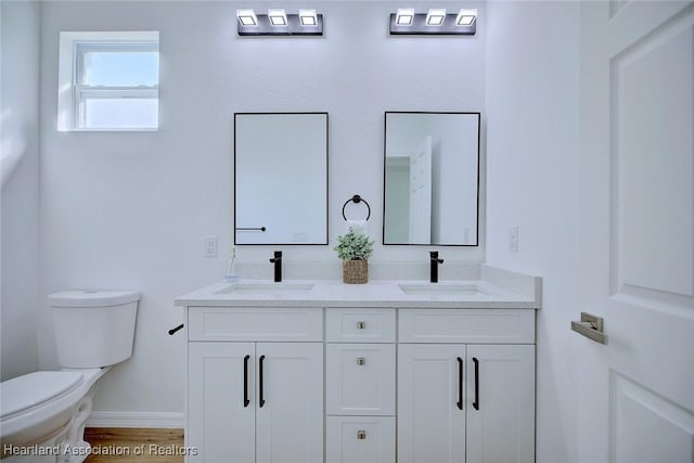bathroom with baseboards, double vanity, a sink, and toilet