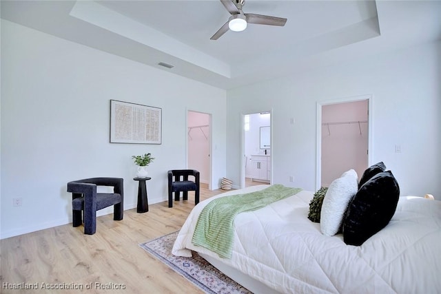 bedroom featuring a closet, visible vents, light wood-style floors, a tray ceiling, and a walk in closet