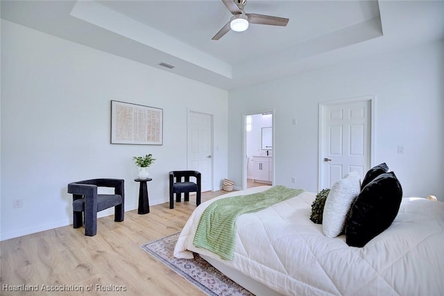 bedroom with a raised ceiling, baseboards, light wood-style flooring, and visible vents