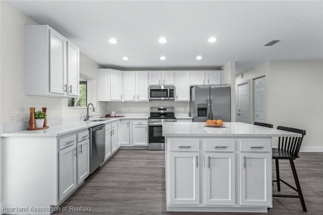 kitchen with appliances with stainless steel finishes, a center island, dark hardwood / wood-style floors, white cabinets, and sink