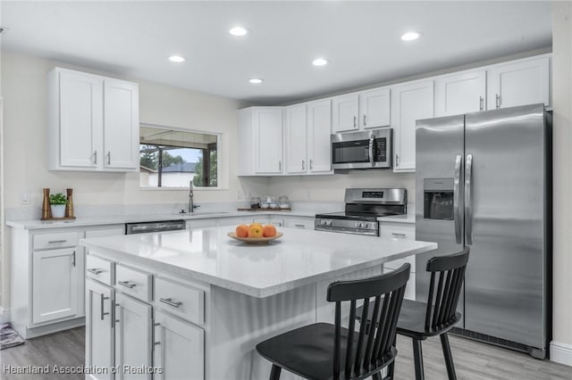 kitchen featuring stainless steel appliances, sink, white cabinets, a kitchen bar, and a kitchen island