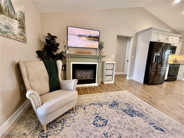 living area featuring light wood-type flooring, lofted ceiling, a fireplace, and baseboards