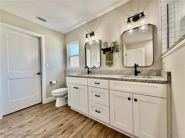 bathroom featuring double vanity, visible vents, a sink, and wood finished floors