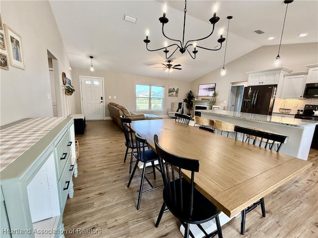 dining area with vaulted ceiling, ceiling fan with notable chandelier, visible vents, and light wood-style floors