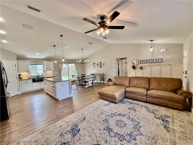 living room with vaulted ceiling, light wood finished floors, ceiling fan with notable chandelier, and visible vents