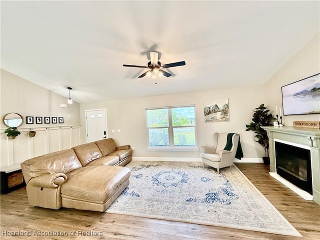 living area with ceiling fan, wood finished floors, baseboards, vaulted ceiling, and a glass covered fireplace