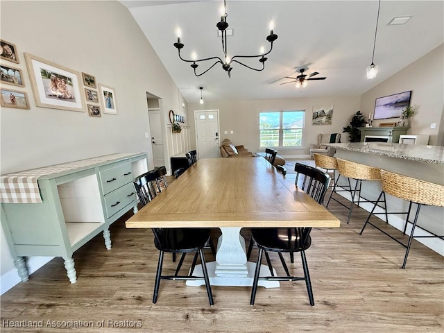 dining room with light wood-style flooring, high vaulted ceiling, and ceiling fan with notable chandelier