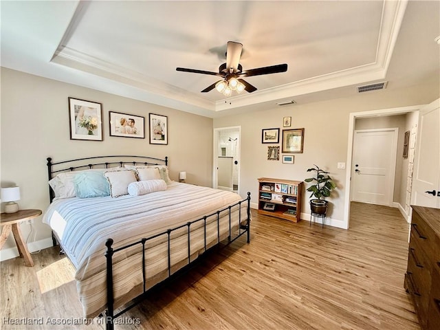 bedroom featuring a raised ceiling, baseboards, crown molding, and light wood finished floors