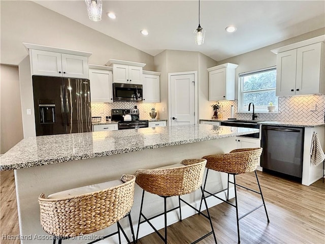 kitchen with black appliances, a kitchen island, white cabinets, and pendant lighting