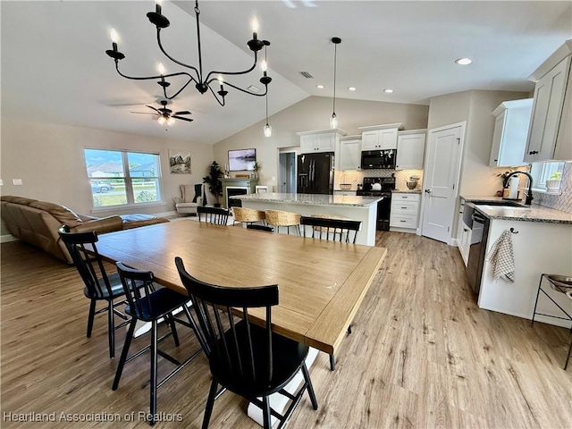 dining area featuring lofted ceiling, light wood-style flooring, visible vents, and ceiling fan with notable chandelier