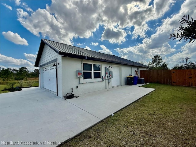 view of property exterior featuring a garage, metal roof, fence, a yard, and stucco siding