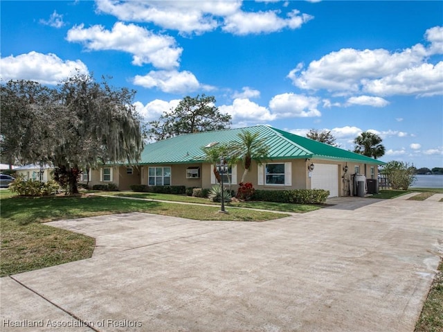 ranch-style house featuring stucco siding, concrete driveway, an attached garage, a front yard, and a standing seam roof