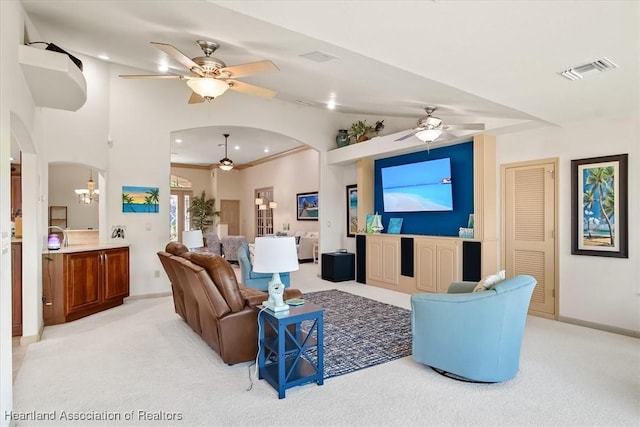 living area featuring light colored carpet, visible vents, a ceiling fan, and arched walkways