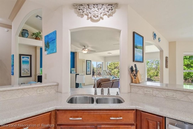 kitchen featuring a ceiling fan, visible vents, arched walkways, a sink, and brown cabinets