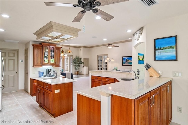 kitchen with glass insert cabinets, ceiling fan, brown cabinets, a peninsula, and a sink