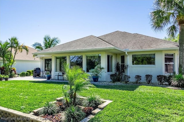 view of front of property with stucco siding, a patio, roof with shingles, and a front lawn