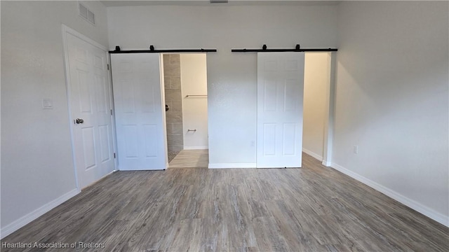 unfurnished bedroom with hardwood / wood-style flooring, ensuite bathroom, and a barn door