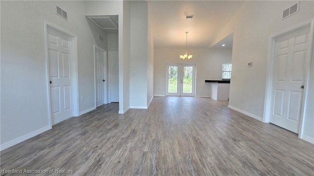 unfurnished living room featuring french doors, a chandelier, and light hardwood / wood-style flooring