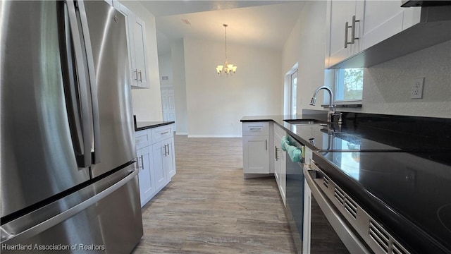 kitchen with appliances with stainless steel finishes, decorative light fixtures, white cabinetry, sink, and light hardwood / wood-style floors