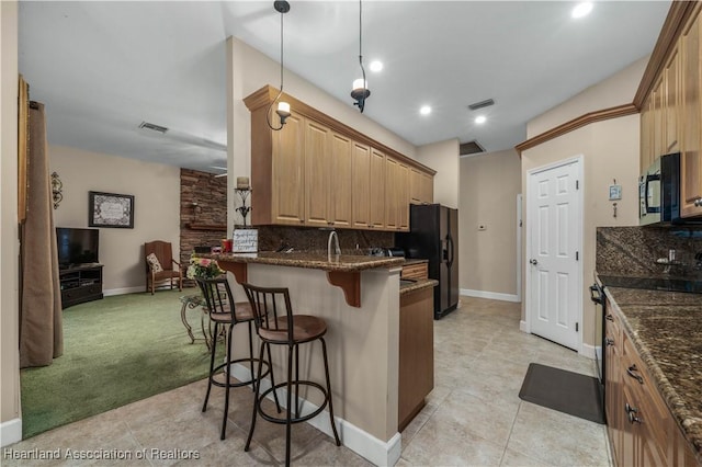 kitchen with pendant lighting, a breakfast bar area, dark stone counters, decorative backsplash, and black refrigerator with ice dispenser