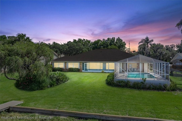 back of property at dusk with a lawn, a lanai, and an outdoor pool