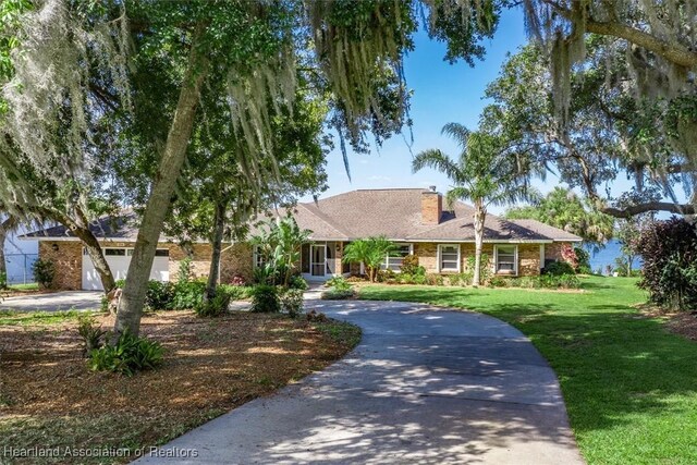 ranch-style house featuring curved driveway, a chimney, a front yard, and a garage