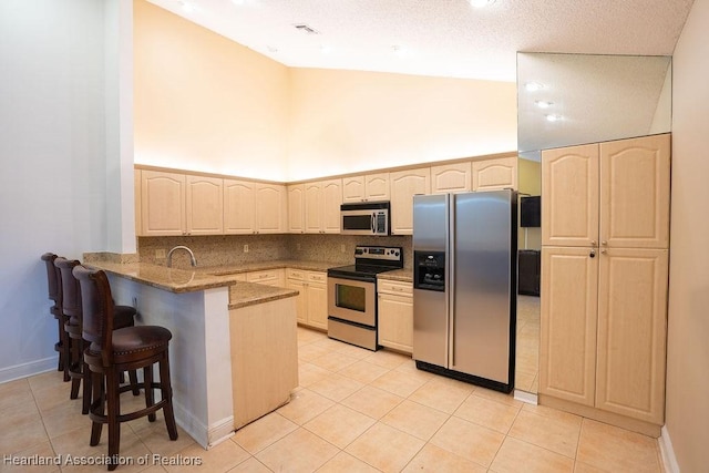 kitchen with kitchen peninsula, high vaulted ceiling, stainless steel appliances, and light tile patterned floors