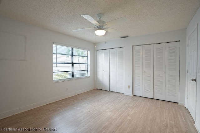 unfurnished bedroom with ceiling fan, light wood-type flooring, a textured ceiling, and multiple closets