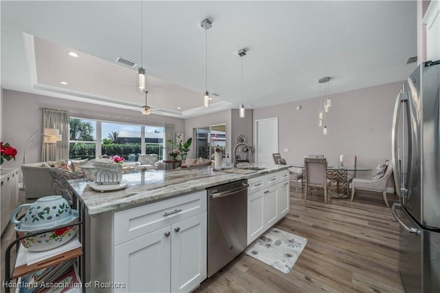 kitchen with stainless steel appliances, a tray ceiling, an island with sink, and white cabinets