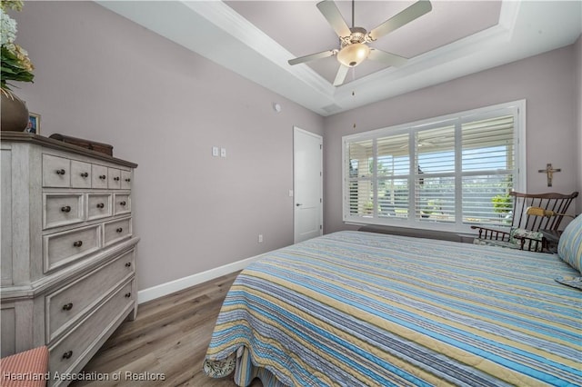 bedroom with wood-type flooring, ornamental molding, a raised ceiling, and ceiling fan