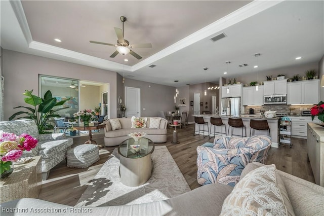 living room with crown molding, hardwood / wood-style floors, a tray ceiling, and ceiling fan