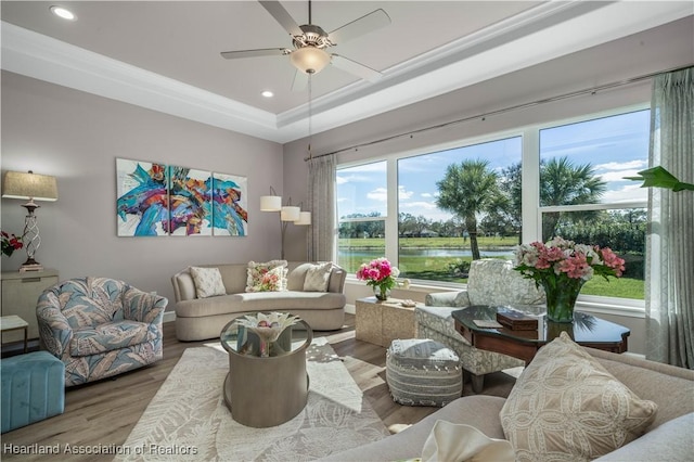 living room with hardwood / wood-style flooring, a water view, ceiling fan, and a tray ceiling